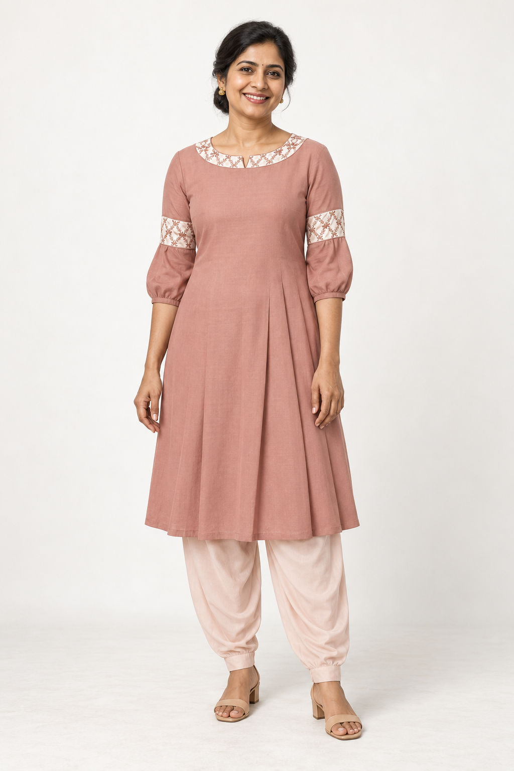 Smiling model wearing a blush kurta with floral lattice bands and light blush salwar trousers